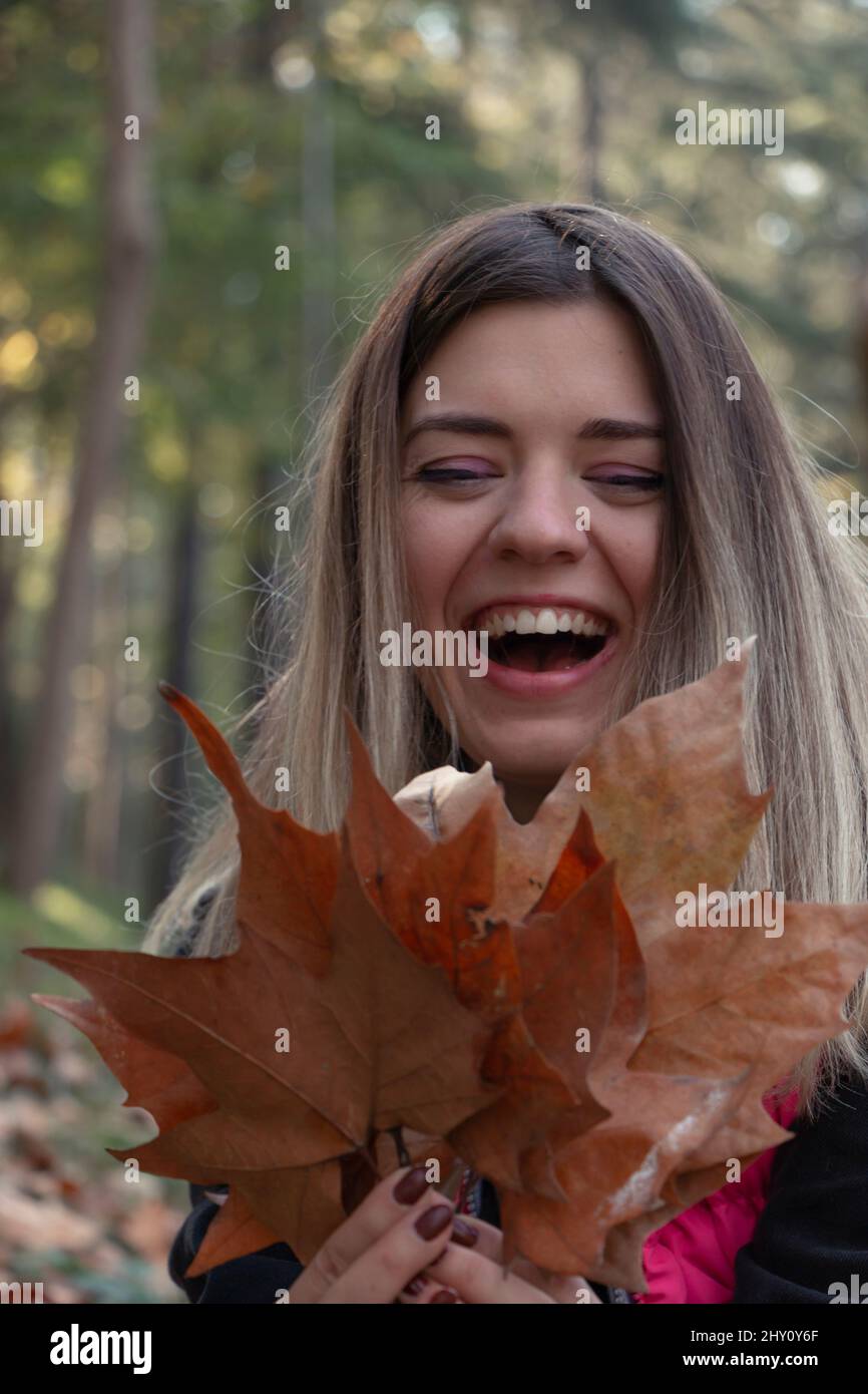 Femme tenant des feuilles d'automne dans la forêt souriant heureux et excité. Portrait d'une fille montrant des feuilles colorées. Feuillage forestier. Femme dans un manteau tendance. Banque D'Images