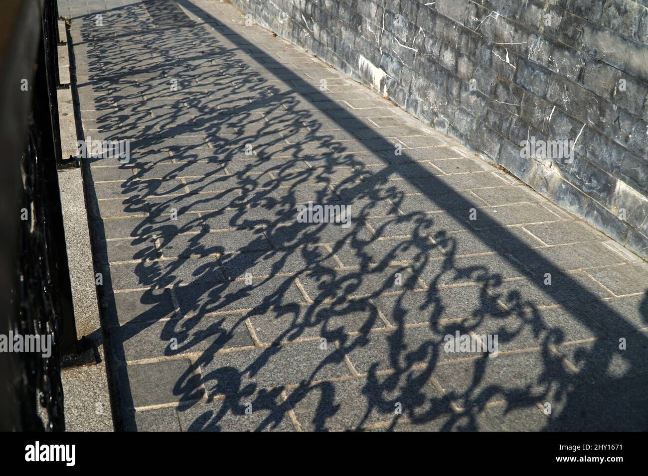Ombres d'une clôture rustique en fer forgé sur un sol en pierre à l'extérieur comme arrière-plan abstrait Banque D'Images