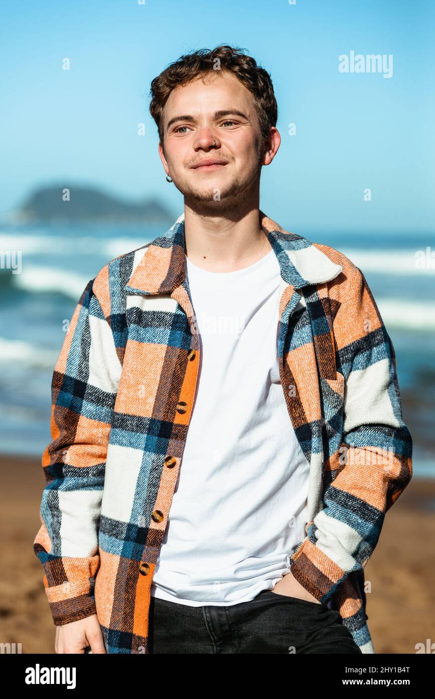 Homme positif en chemise à carreaux debout sur la côte près de la mer agitant dans la zone côtière Banque D'Images