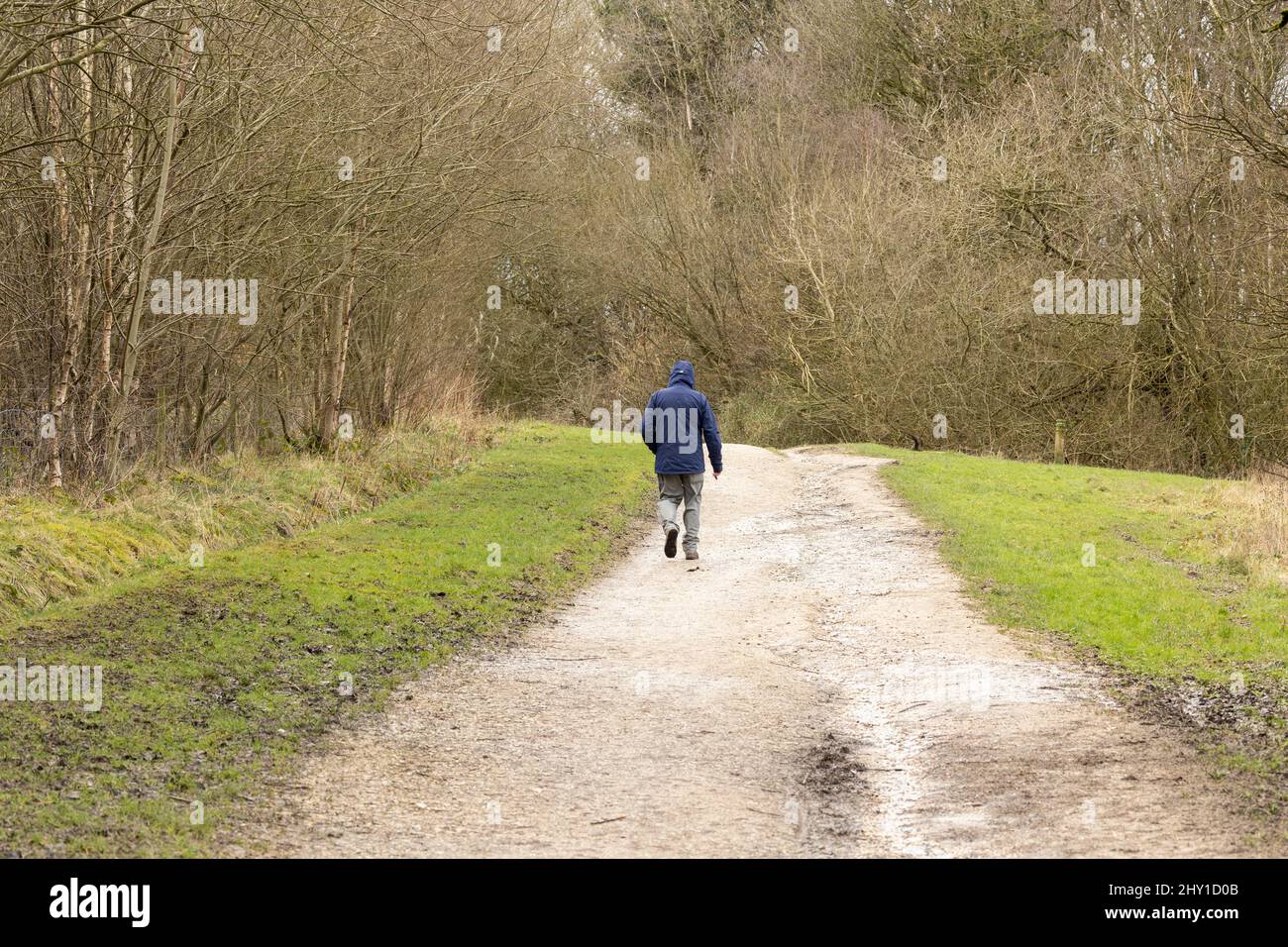 un homme seul portant un sweat à capuche marchant le long d'une piste de terre dans la campagne d'hiver orientation paysage Banque D'Images