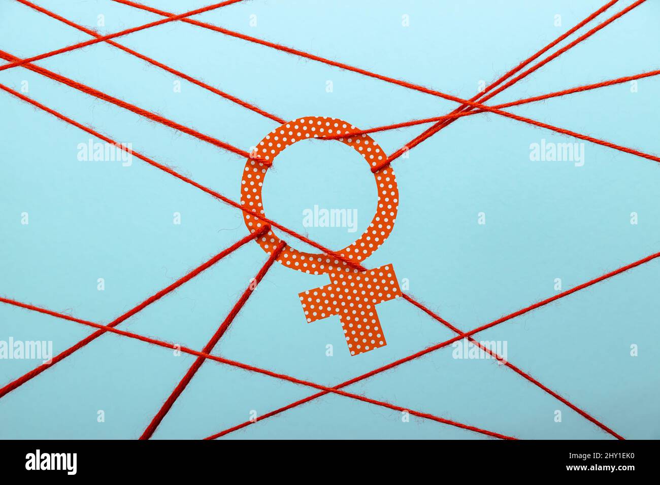 Symbole de Vénus à point de polka orange attaché avec des cordes représentant l'inégalité des sexes sur fond bleu Banque D'Images