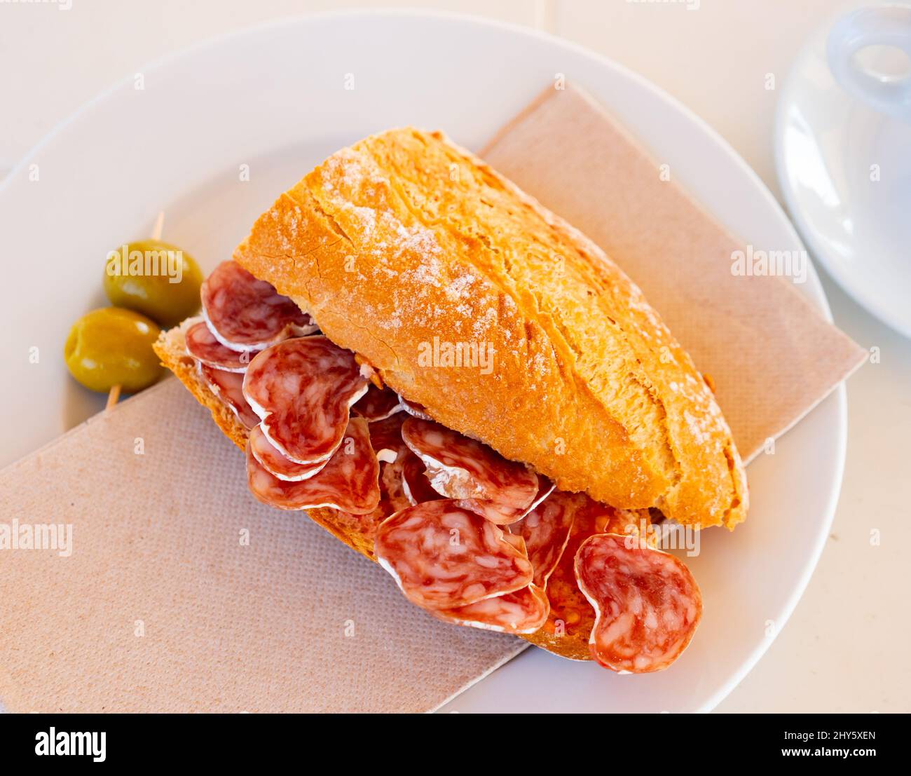 Petit-déjeuner espagnol - sandwich au fuet aux saucisses fumées et olives en gros plan Banque D'Images