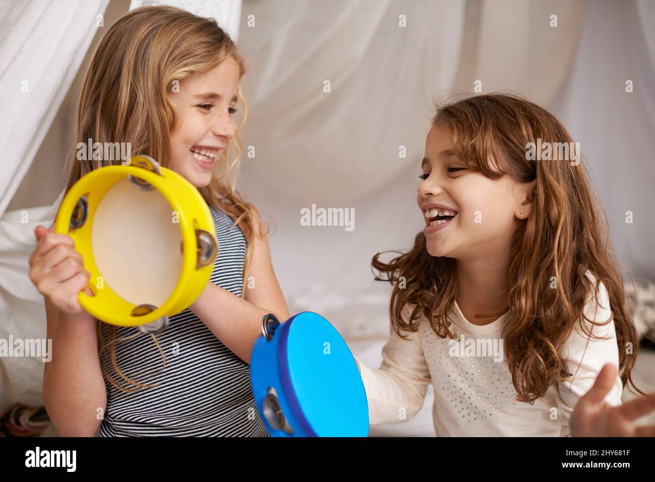 Musique et joie. Photo de deux jolies petites filles jouant avec des tambourins à la maison. Banque D'Images