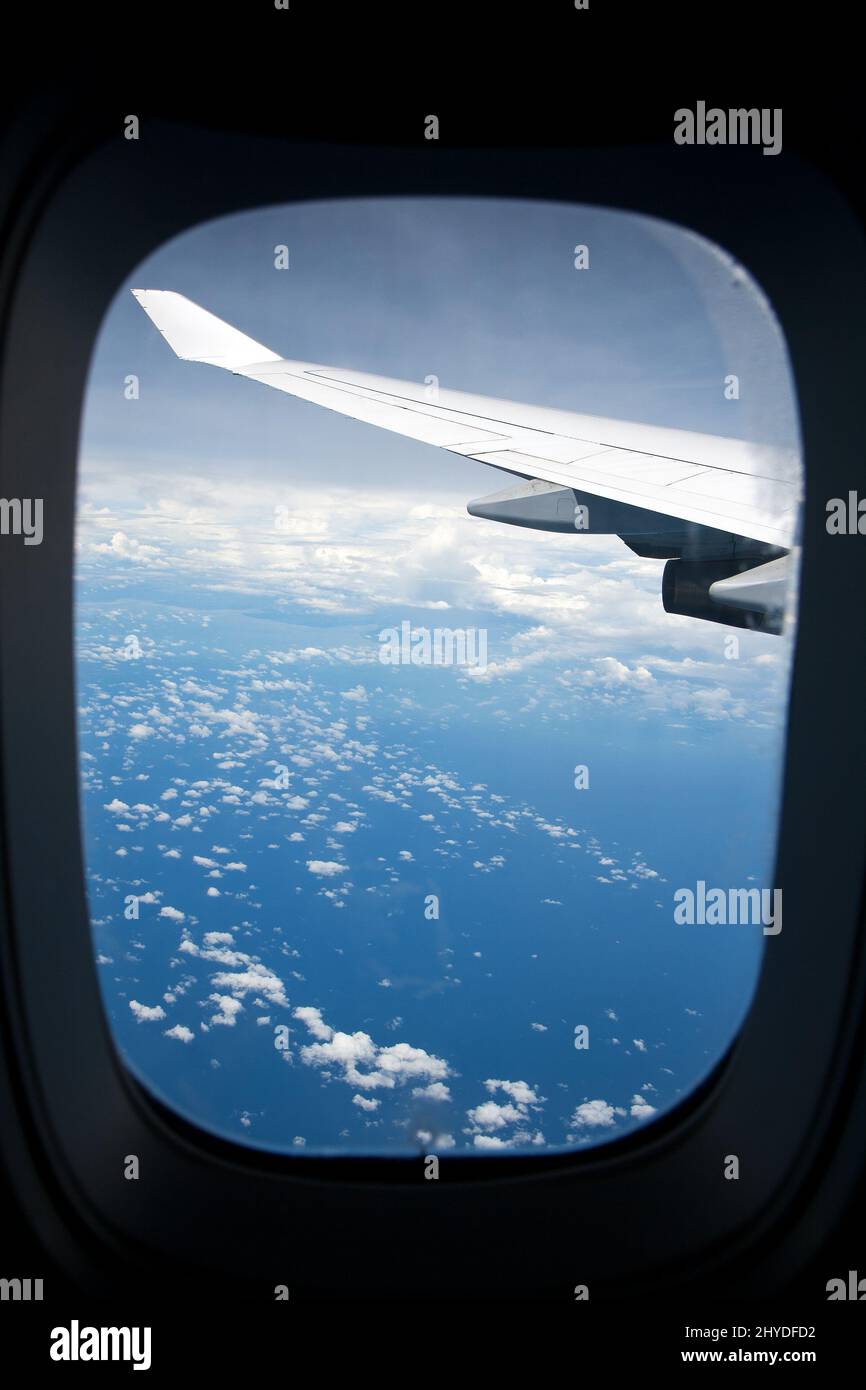 Voler au-dessus des nuages. Ciel bleu, nuages et aile d'avion au-dessus de l'océan vue par une fenêtre par une journée ensoleillée. Banque D'Images