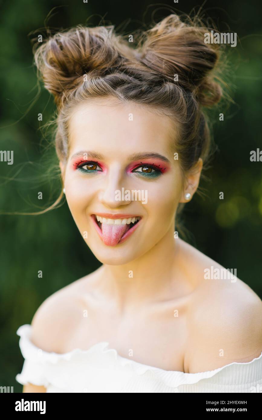 Une jeune fille ou une jeune fille joyeuse avec un maquillage brillant et une coiffure drôle a pillé un oeil et montre une langue souriante Banque D'Images