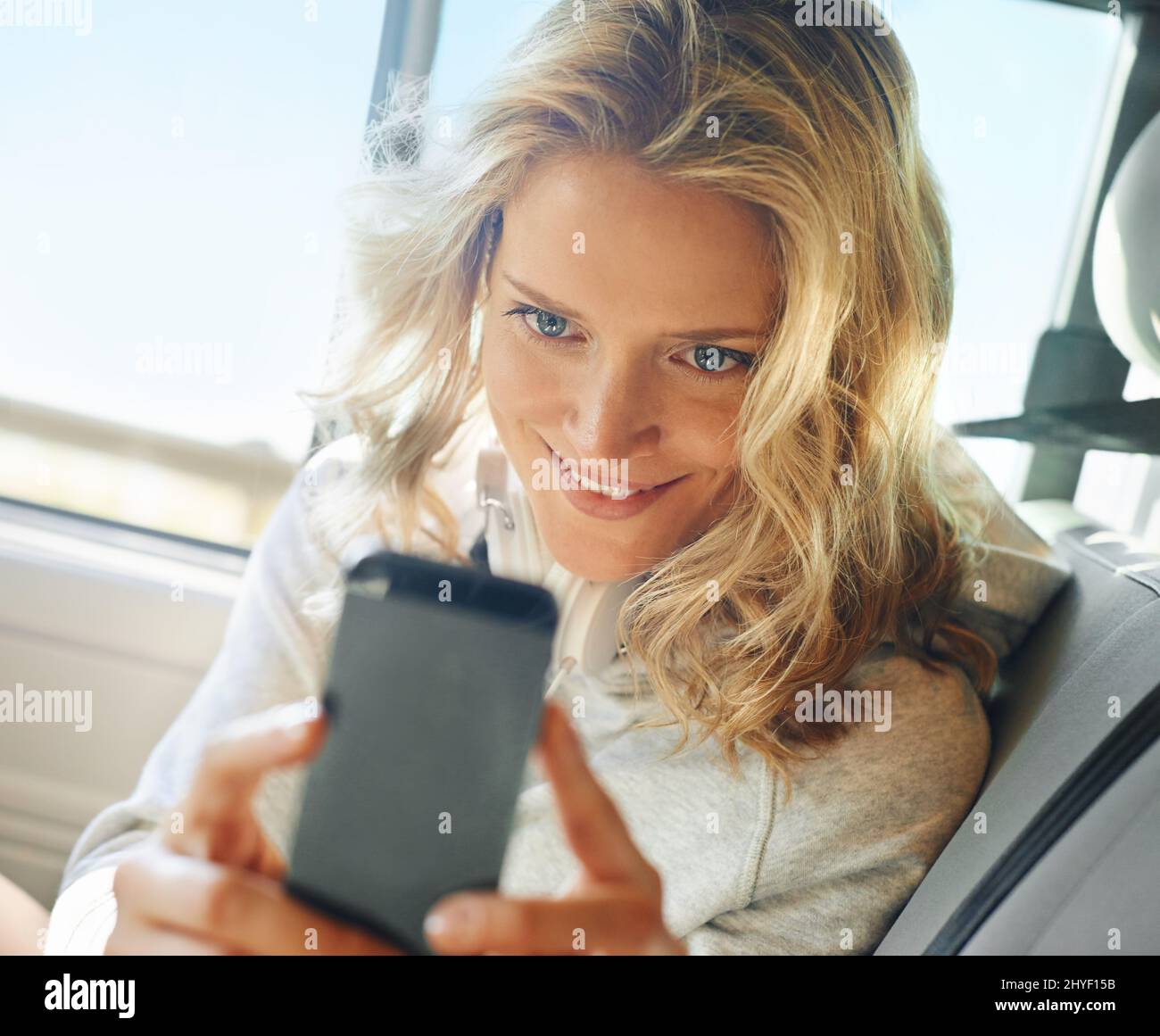 Prise d'une photo rapide. Photo d'une fille souriante prenant un autoportrait sur son téléphone alors qu'elle est assise dans sa voiture. Banque D'Images