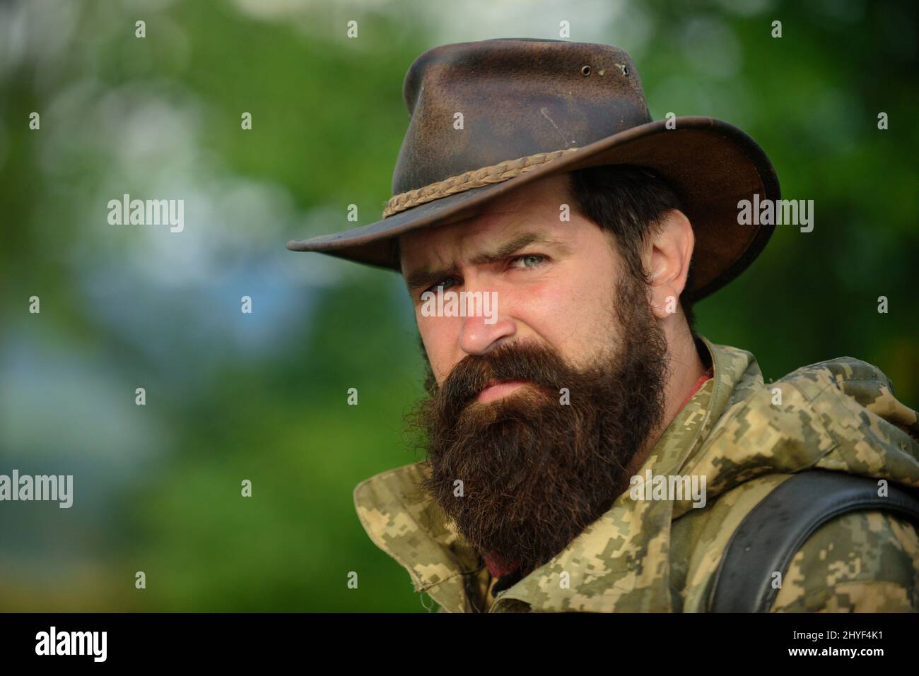 Portrait d'un bel homme barbu avec un visage sérieux et un chapeau de cow-boy en plein air. Gros plan sur le visage masculin. Banque D'Images