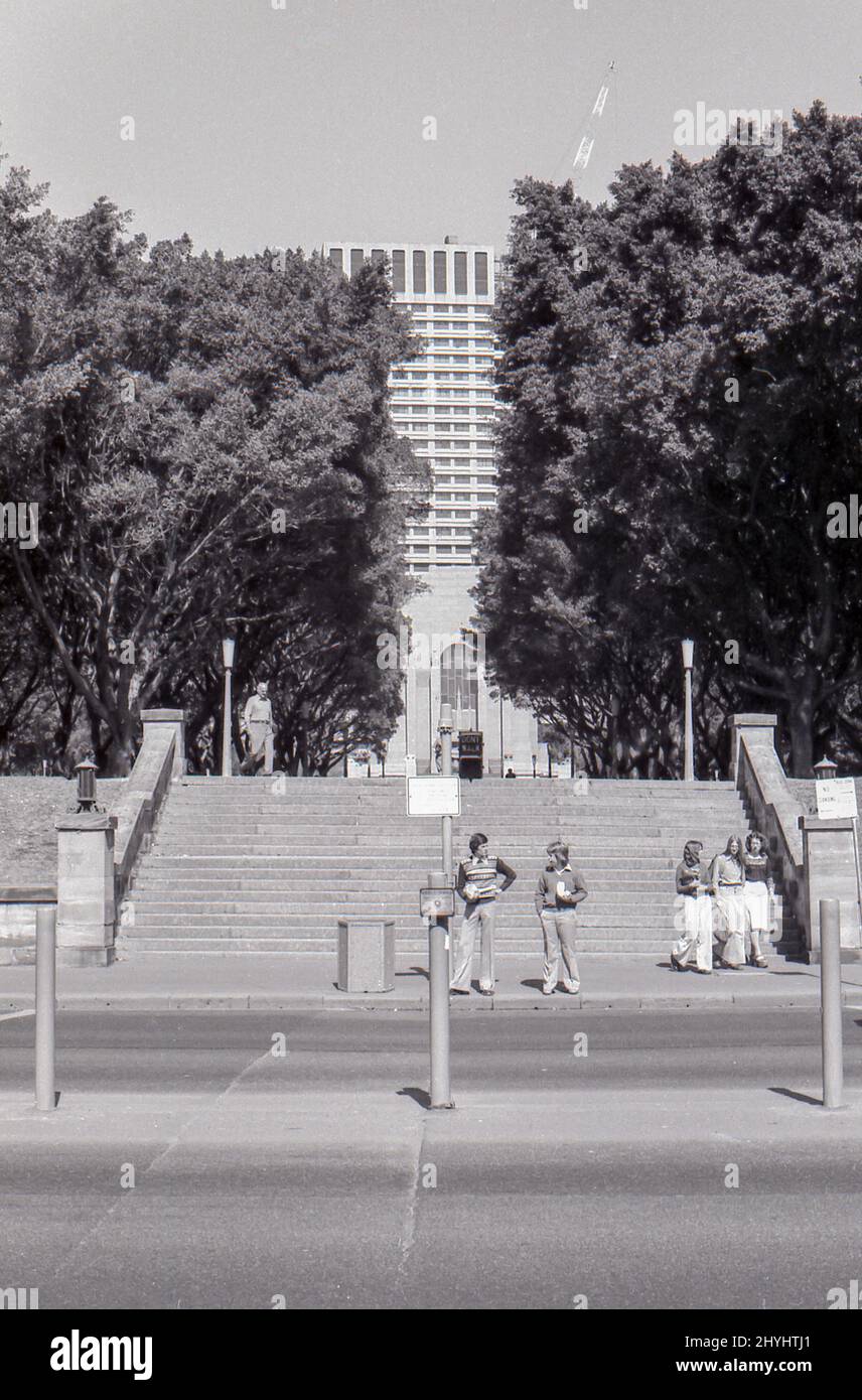Sydney Australia 1977 : vue depuis la partie nord de Hyde Park, en face de Park Street, jusqu'aux escaliers et au chemin central qui mène jusqu'à Liverpool Street à Sydney. En 2022, le diviseur de route central (premier plan) a disparu et les arbres remplissent maintenant l'espace qui cache ainsi le bâtiment au 175 Liverpool Street, et les tenues ont changé, mais sinon peu a changé. Banque D'Images