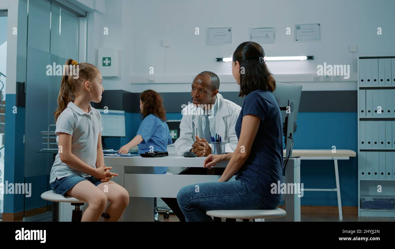 Médecin saluant la petite fille et la mère dans le cabinet médical. Médecin et patient de sexe masculin ayant une conversation sur la maladie et le traitement sur ordonnance lors de la visite de contrôle annuelle. Service de santé Banque D'Images