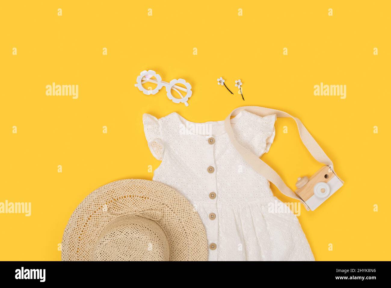 Ensemble de vêtements d'été élégants pour enfants. Robe blanche, chapeau de paille, lunettes de soleil et accessoires sur fond jaune. Mode fille Lookbook concept. Haut v Banque D'Images
