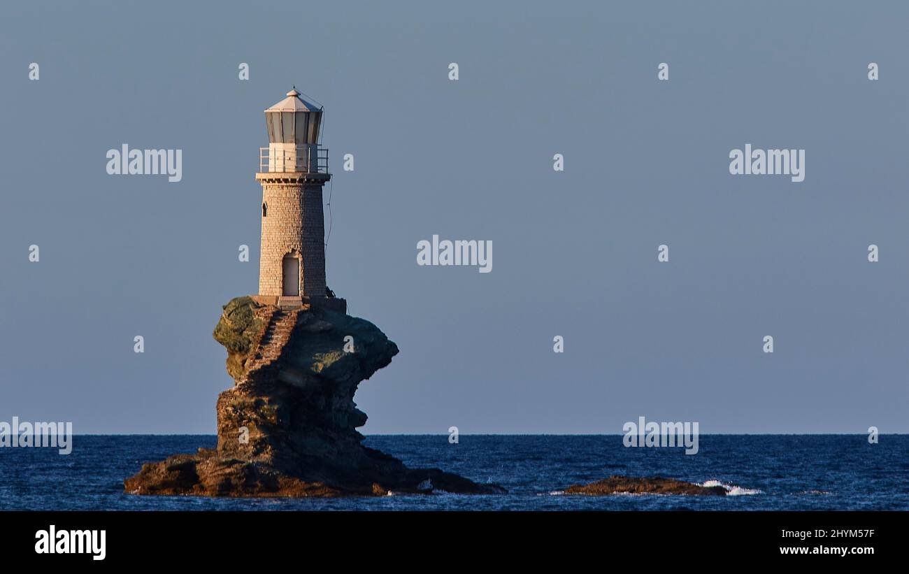 Téléobjectif, phare rond blanc sur la roche proche, bleu foncé de mer, bleu ciel clair et sans nuages, ville d'Andros, Chora, île d'Andros, Cyclades, Grèce Banque D'Images