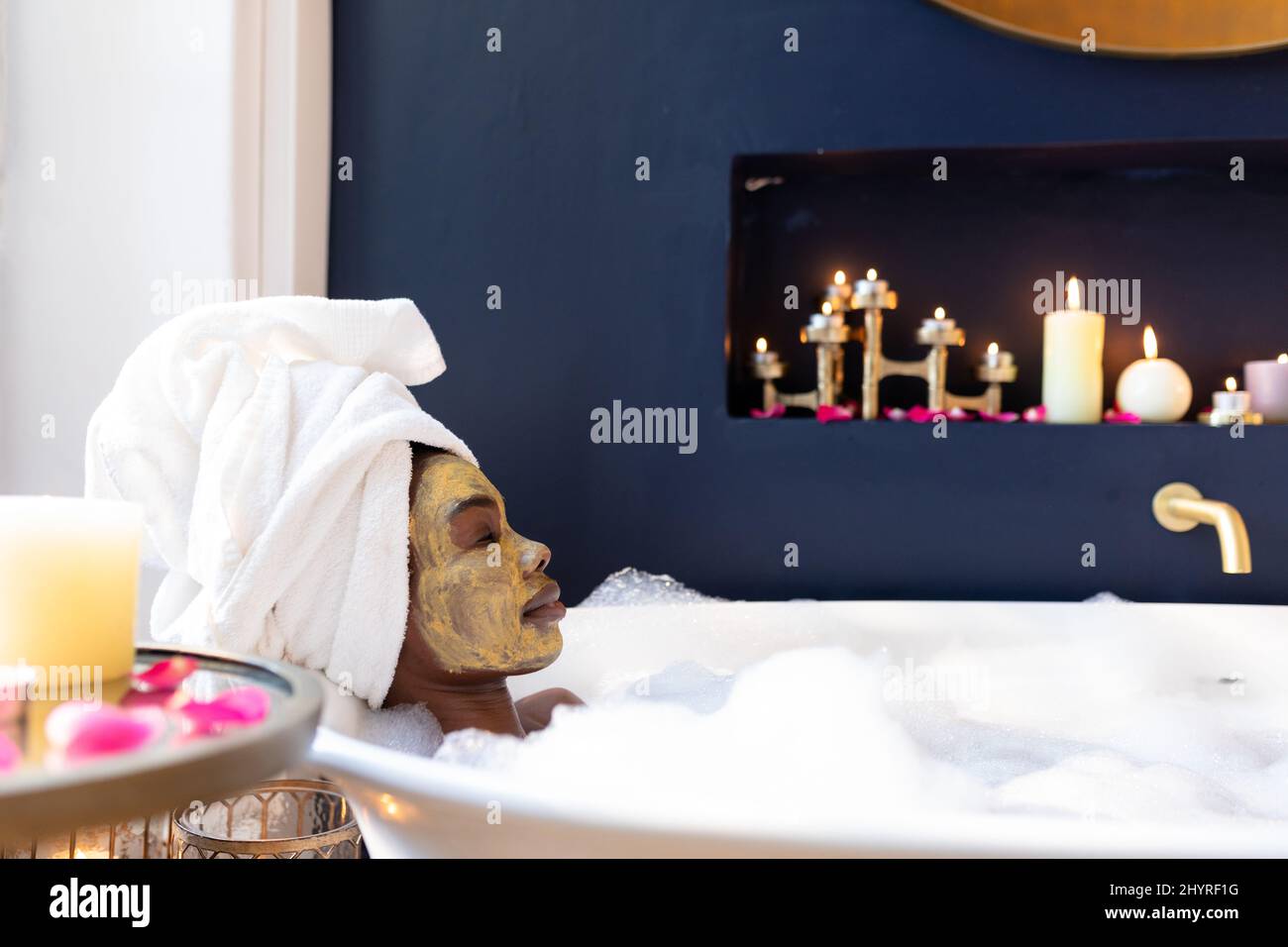 Femme afro-américaine décontractée avec masque dans la baignoire avec des bulles à la maison Banque D'Images