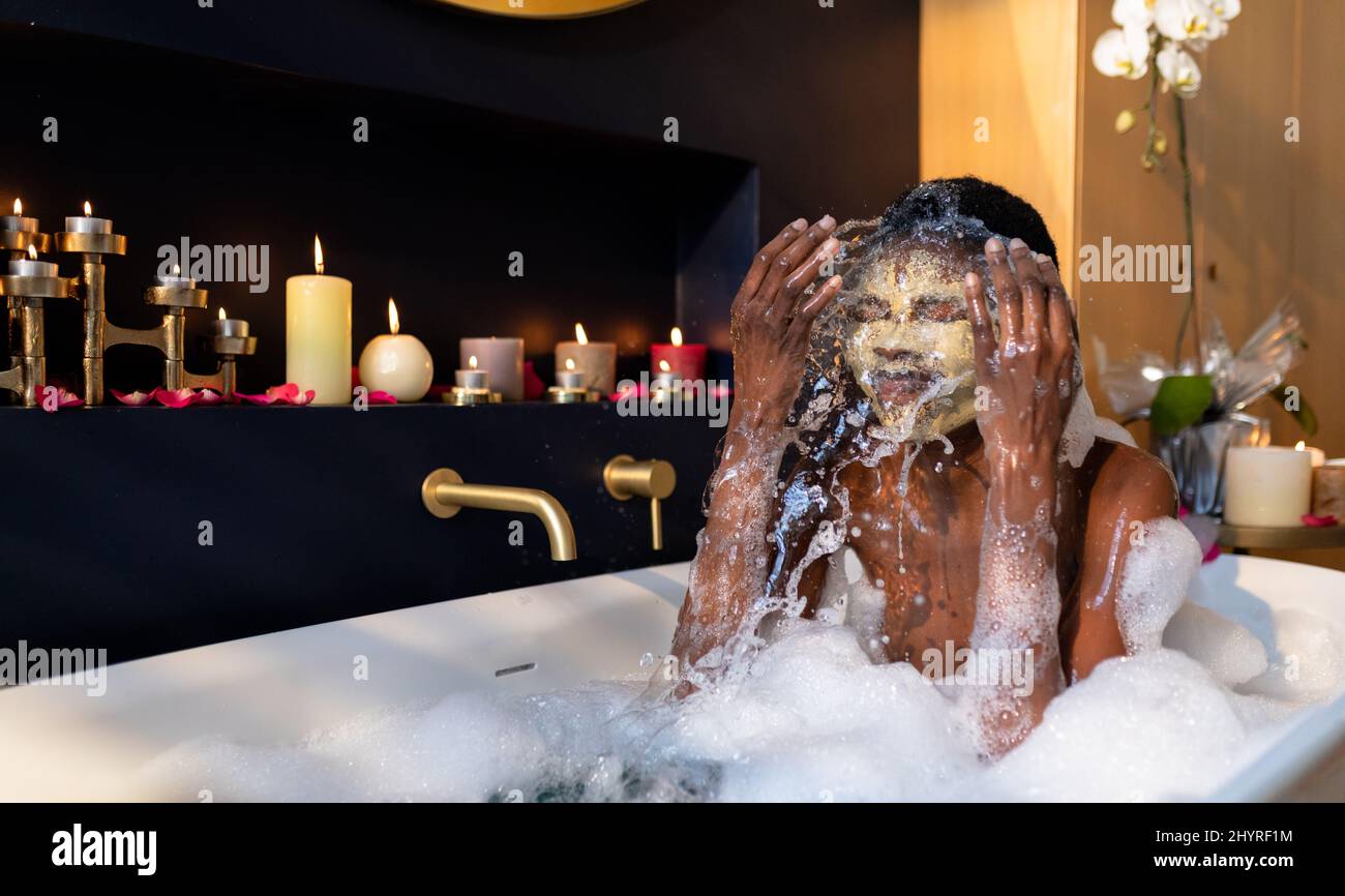 Femme afro-américaine barbotant de l'eau tout en lavant le masque dans la baignoire Banque D'Images