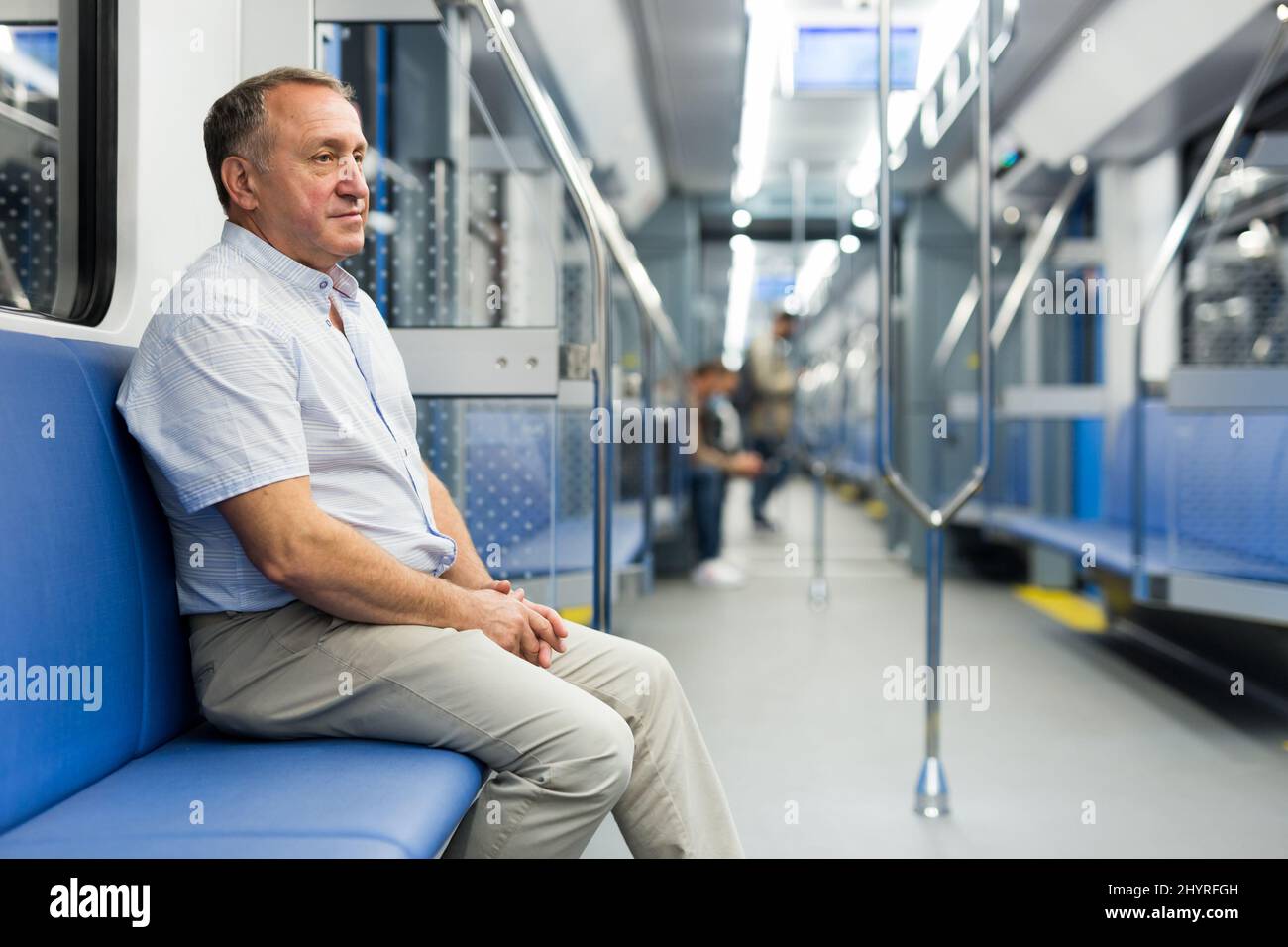 Homme âgé positif assis dans une voiture de métro vide pendant que le train est en mouvement Banque D'Images