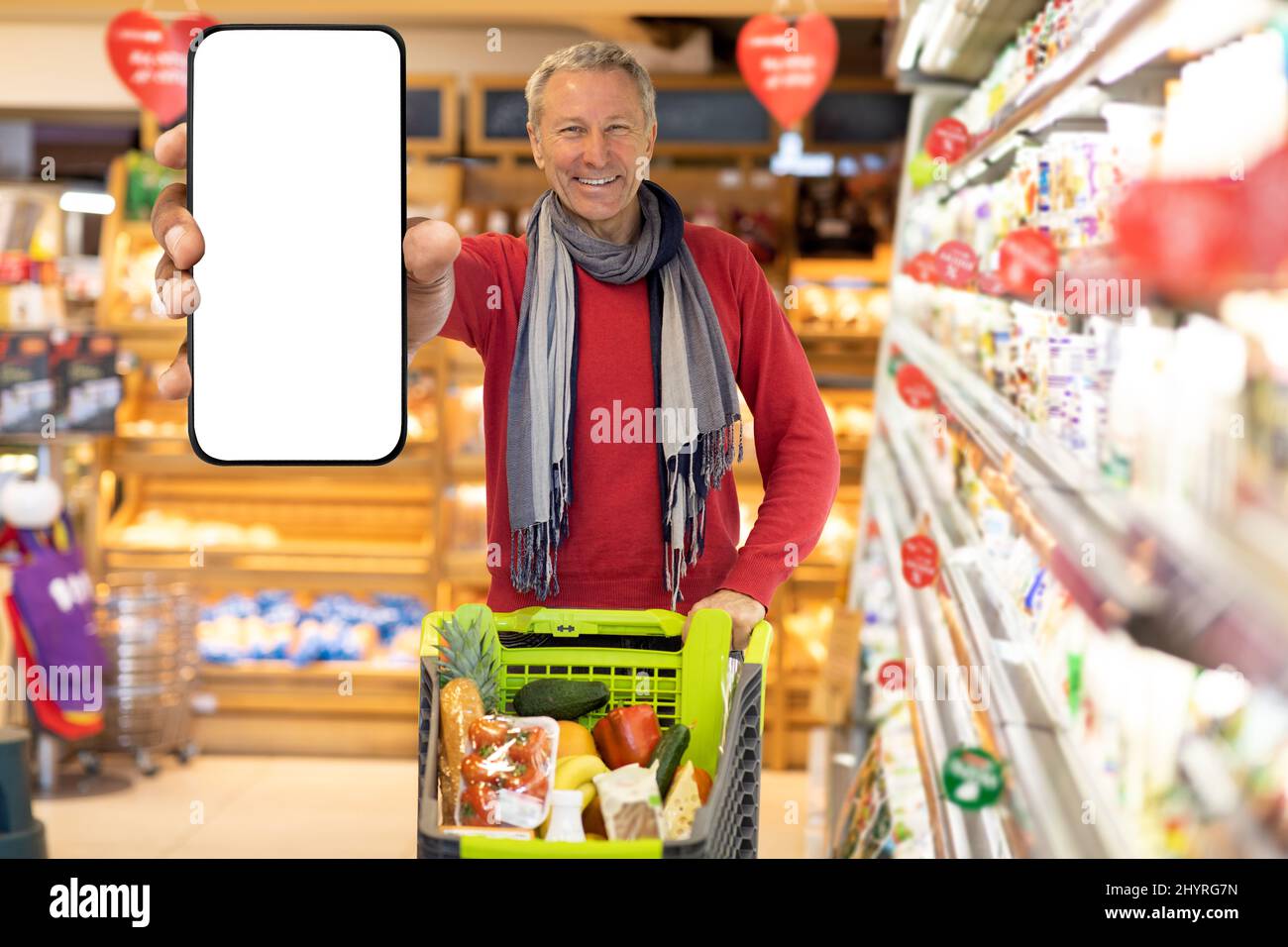 Joyeux homme âgé magasiner au supermarché, montrant le smartphone, mockup Banque D'Images