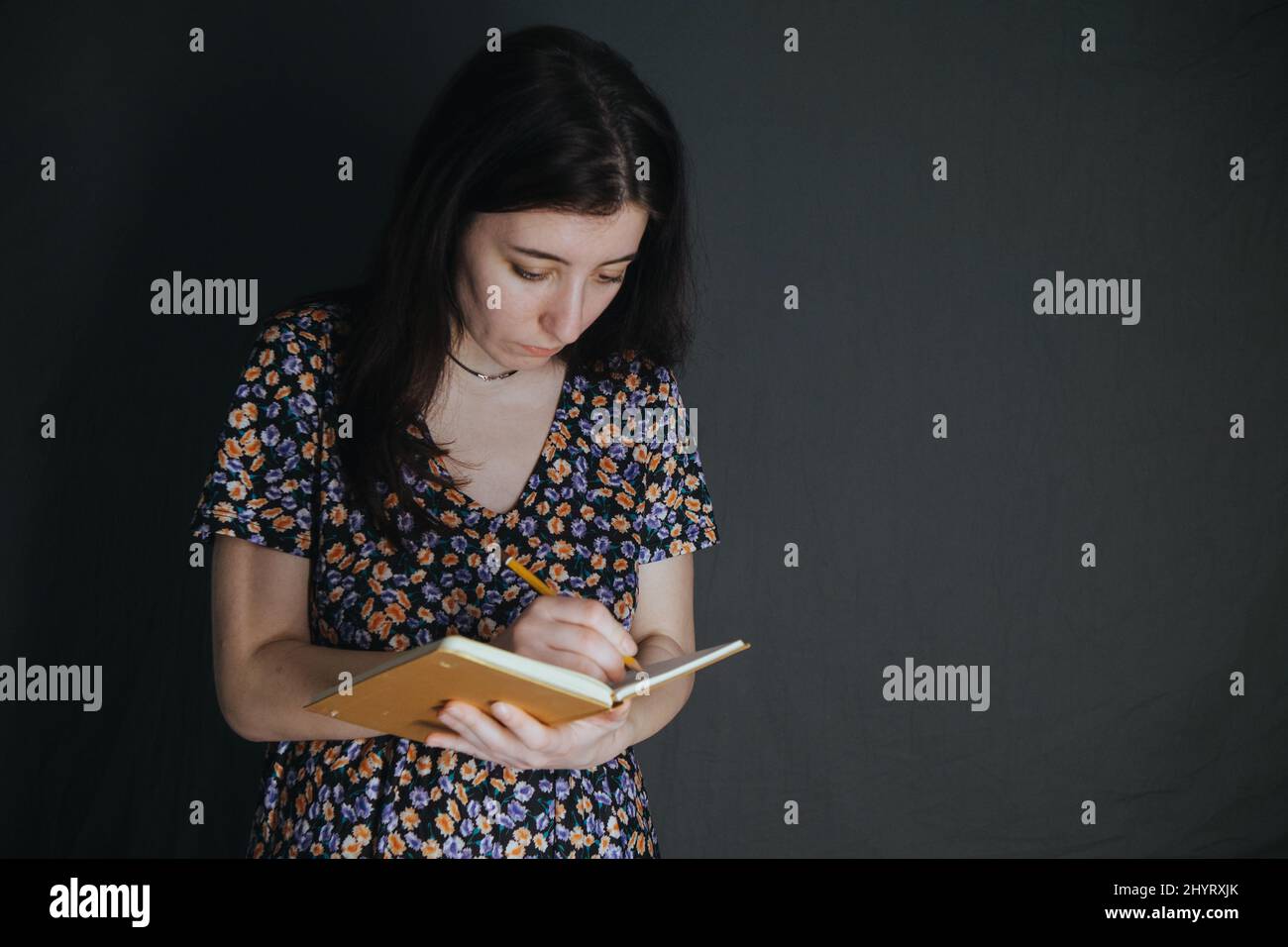 une jeune femme arménienne ukrainienne prend des notes avec un stylo dans son carnet sur fond gris Banque D'Images