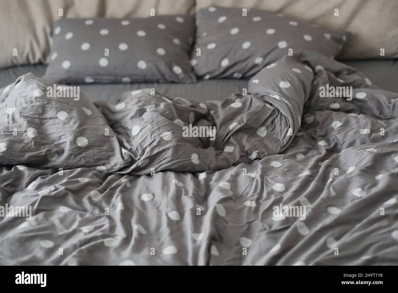 le matin, un lit désordonné avec une couverture et des oreillers gris Banque D'Images