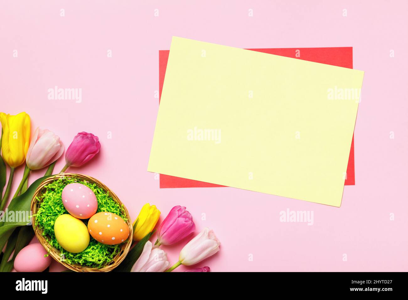 Carte de Pâques. Oeufs dans un panier fleurs tulipes feuille de papier vide avec place pour le texte sur fond rose. Banque D'Images
