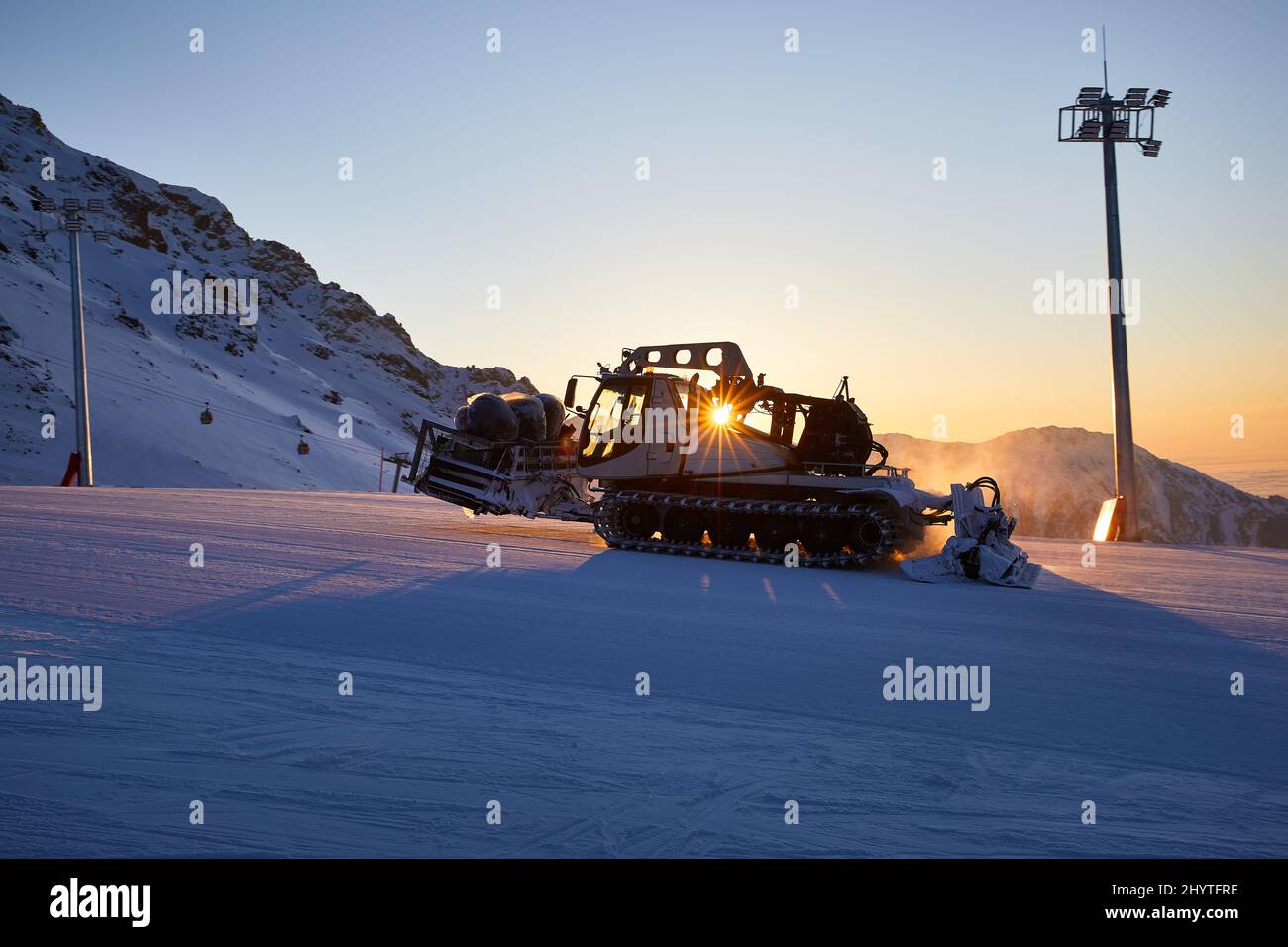 Silhouette de ratrack moderne de chat de neige avec chasse-neige préparant la piste de ski avec étoile lumineuse au soleil à la station de ski de Shymbulak Almaty, Kazakhstan Banque D'Images