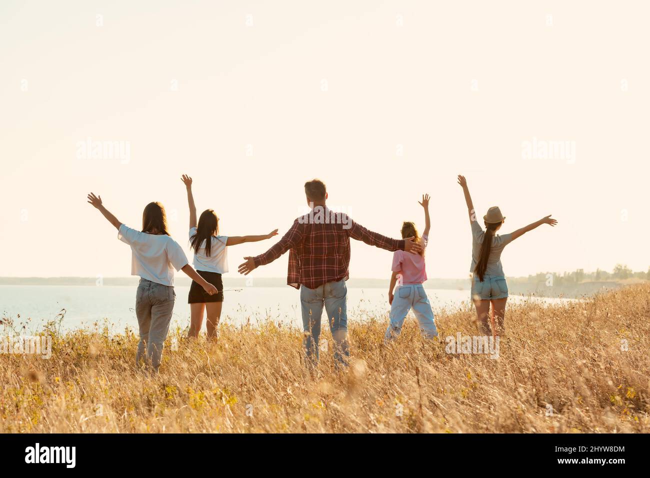 Groupe d'amis heureux se tient avec les bras levés au coucher du soleil Banque D'Images Groupe d'amis heureux se tient avec les bras levés au coucher du soleil Banque D'Images