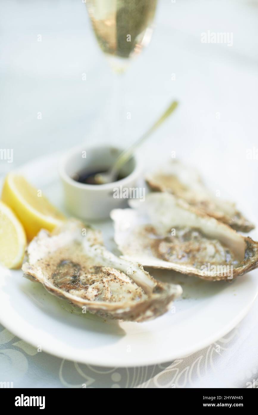 Et pour commencer Photo d'une assiette d'huîtres assise sur une table avec un verre de vin. Banque D'Images