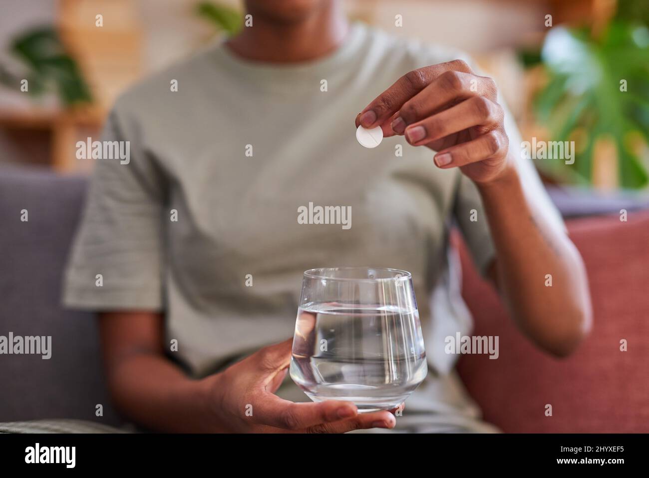 Une jeune femme dépose un comprimé effervescent fuzzy dans un verre d'eau pour la grippe Banque D'Images