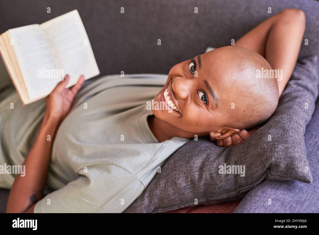Une jeune femme sourit et lit un roman à la maison sur le canapé Banque D'Images