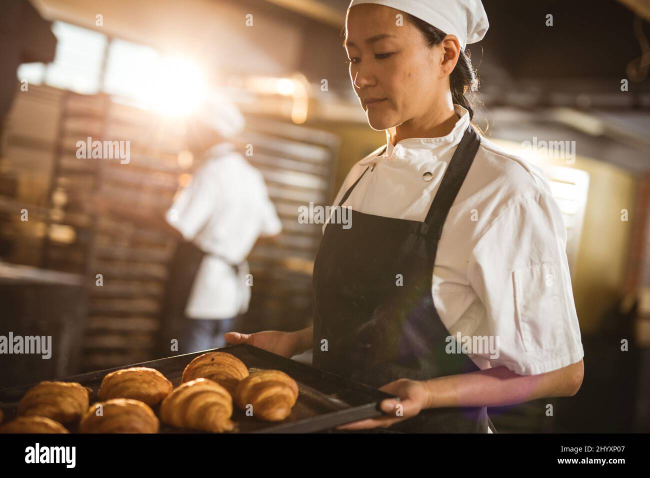 Boulanger asiatique moyen adulte tenant une plaque de cuisson avec croissant tout en travaillant dans la boulangerie Banque D'Images