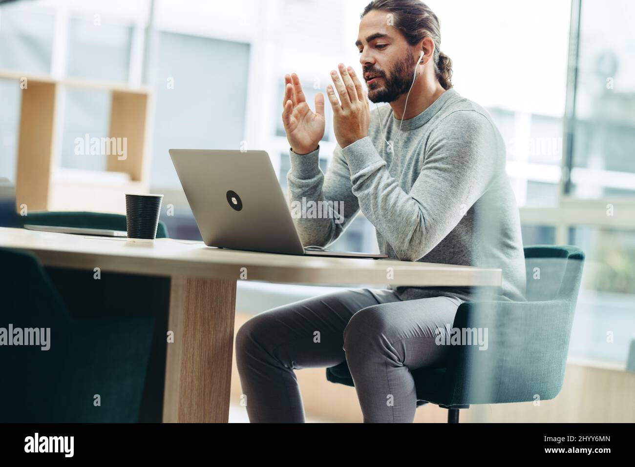 Jeune homme d'affaires ayant une discussion avec ses associés au cours d'une réunion virtuelle. Homme d'affaires moderne assistant à une visioconférence tout en travaillant à remo Banque D'Images