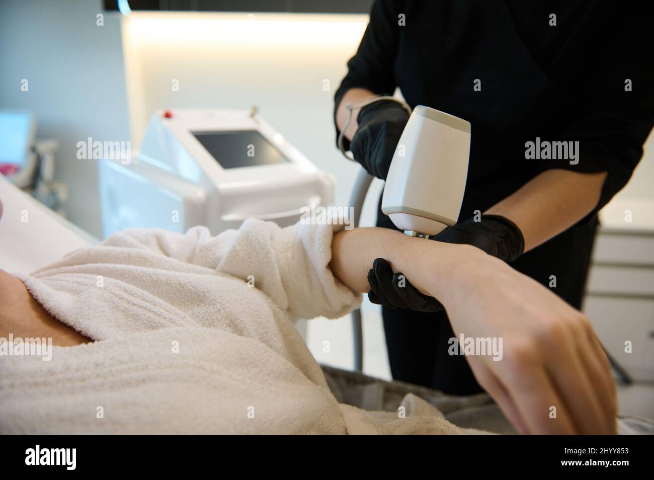 Gros plan d'une esthéticienne cosmétologue méconnaissable effectuant une procédure d'enlèvement de cheveux sur la main d'une femme avec l'équipement laser moderne en wel Banque D'Images