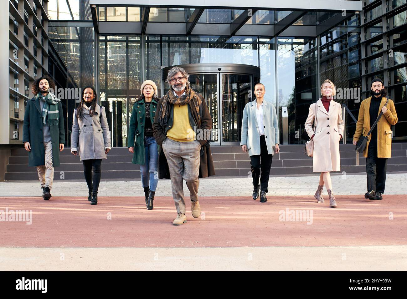 Un groupe multiethnique de gens d'affaires joyeux marchant vers la caméra à l'extérieur d'un centre d'affaires. Banque D'Images