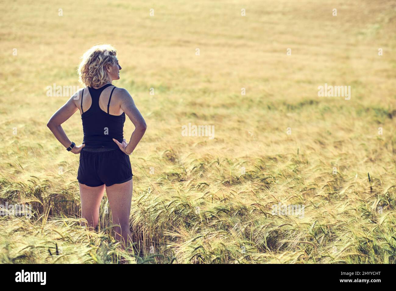 Portrait arrière d'une jeune femme caucasienne adulte avec des cheveux blonds dans des vêtements de sport en plein air dans un paysage de céréales agricoles. Concept de style de vie. Banque D'Images