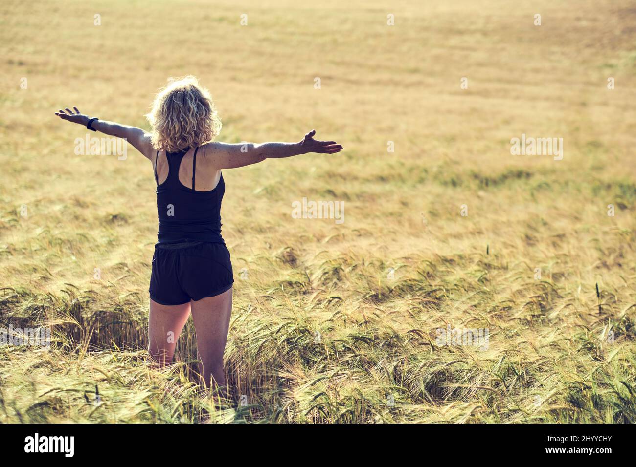 Portrait arrière d'une jeune femme caucasienne adulte avec des cheveux blonds dans des vêtements de sport en plein air dans un paysage de céréales agricoles. Concept de style de vie. Banque D'Images