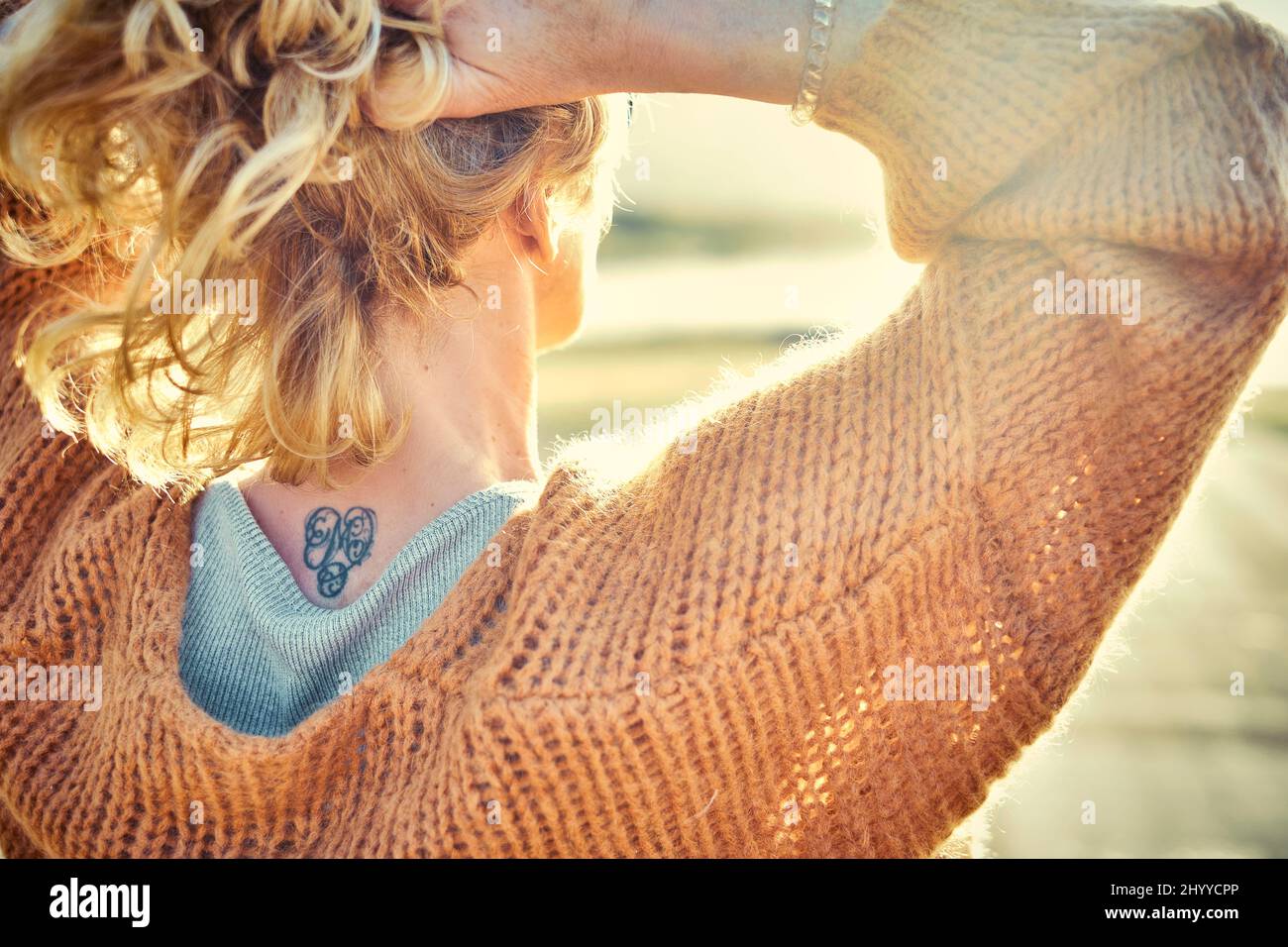 Vue arrière d'une jeune femme blanche blonde avec un tatouage dans est nape à l'extérieur dans un secteur de plage dans une journée ensoleillée. Plage de Berria, Cantabrie, Espagne, Europe. Banque D'Images
