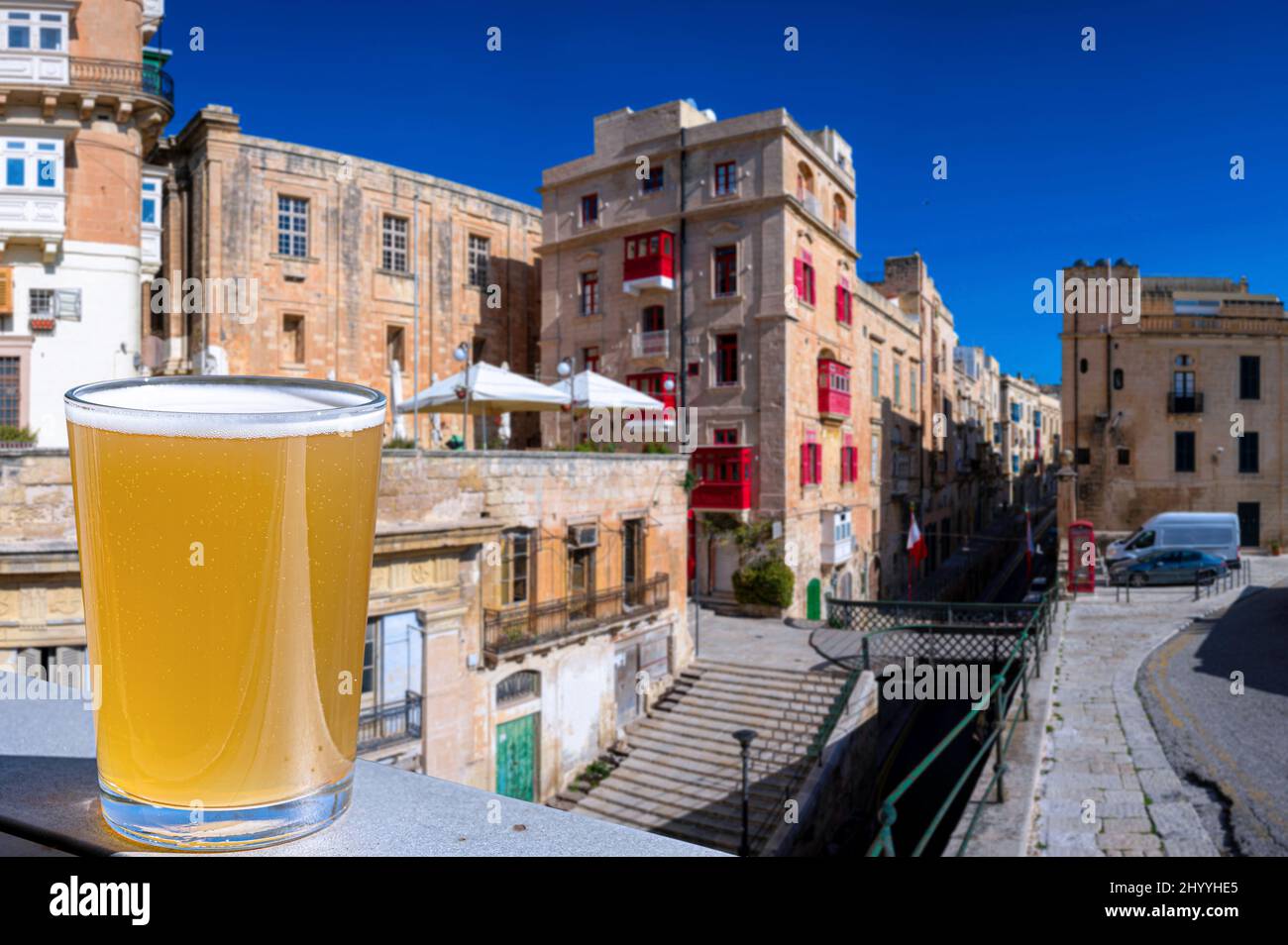 Verre de bière légère avec vue sur la passerelle et la rue étroite avec des escaliers à la Valette, Malte. Banque D'Images