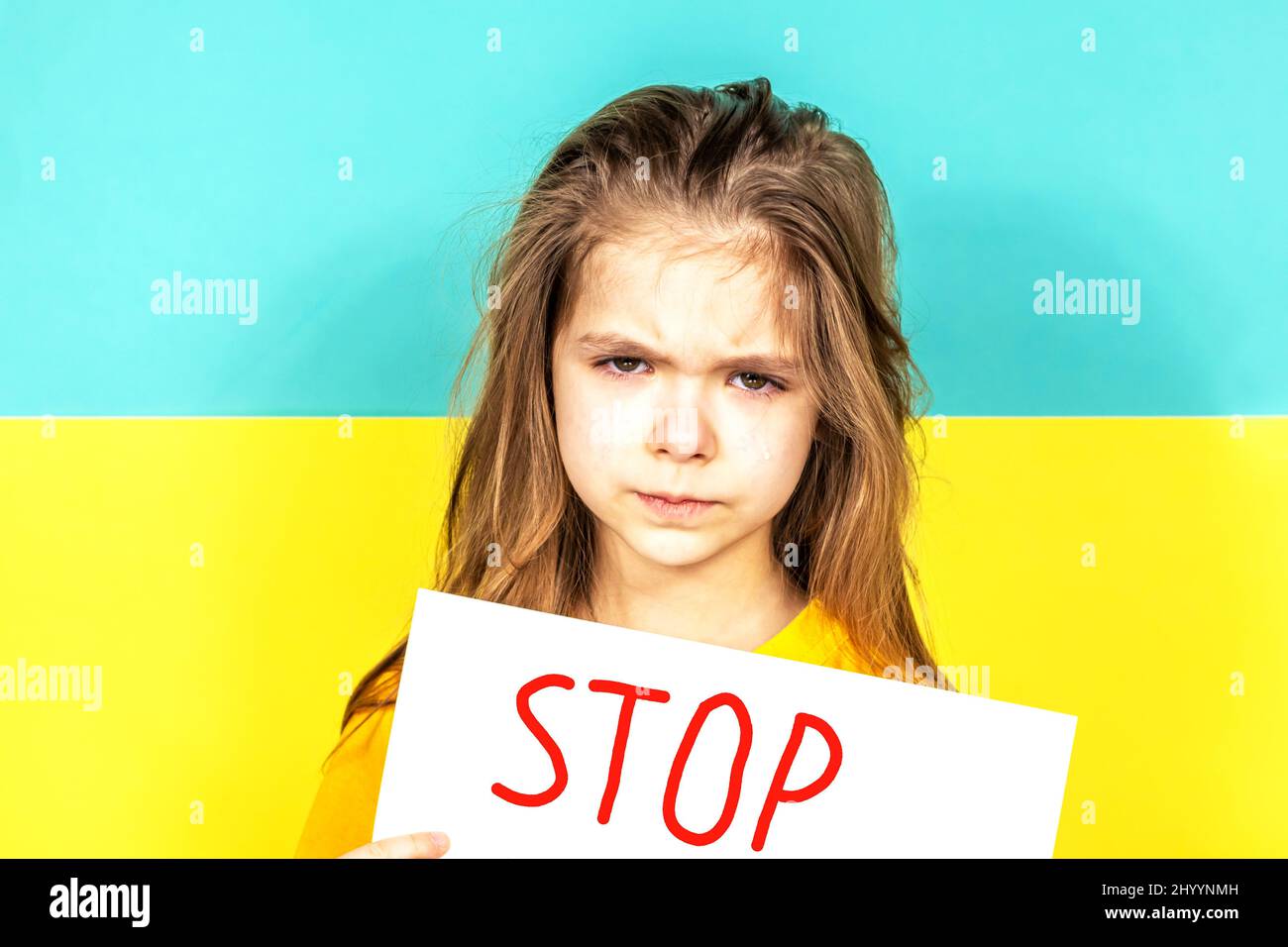 Le visage d'une fille qui pleure en gros plan. La fille tient une AFFICHE D'ARRÊT dans ses mains contre le fond du drapeau ukrainien. Arrêter la guerre en Ukraine Banque D'Images