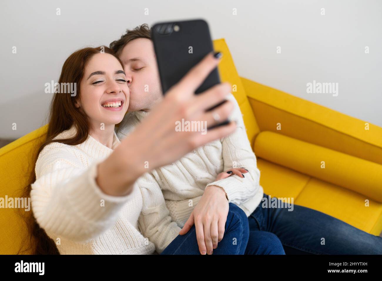 un jeune couple marié à la maison. Ils s'assoient sur le canapé et prennent des selfies Banque D'Images