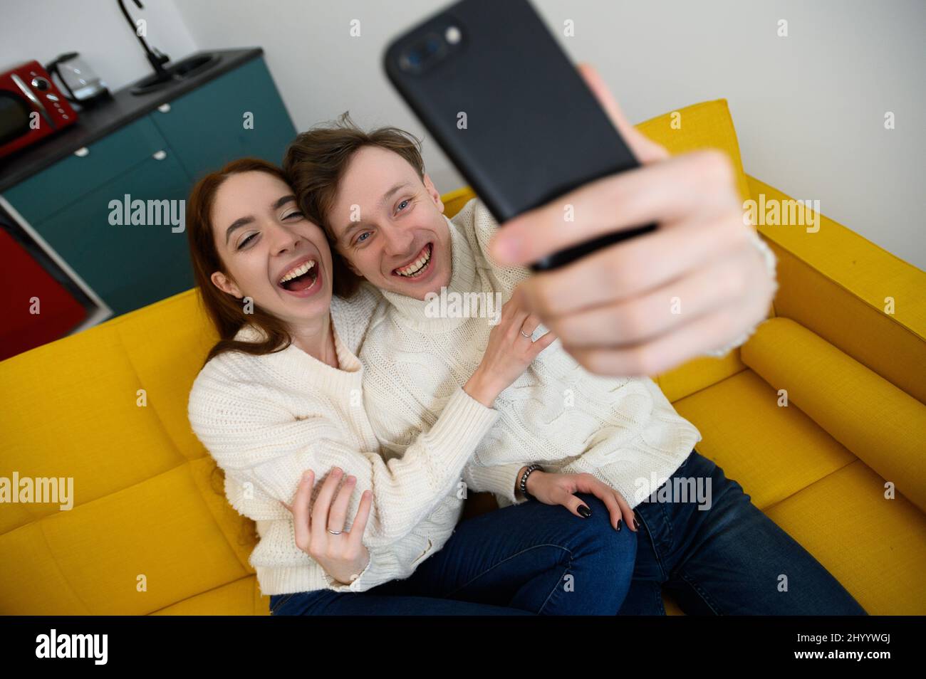 un jeune couple marié à la maison. Ils s'assoient sur le canapé et prennent des selfies Banque D'Images
