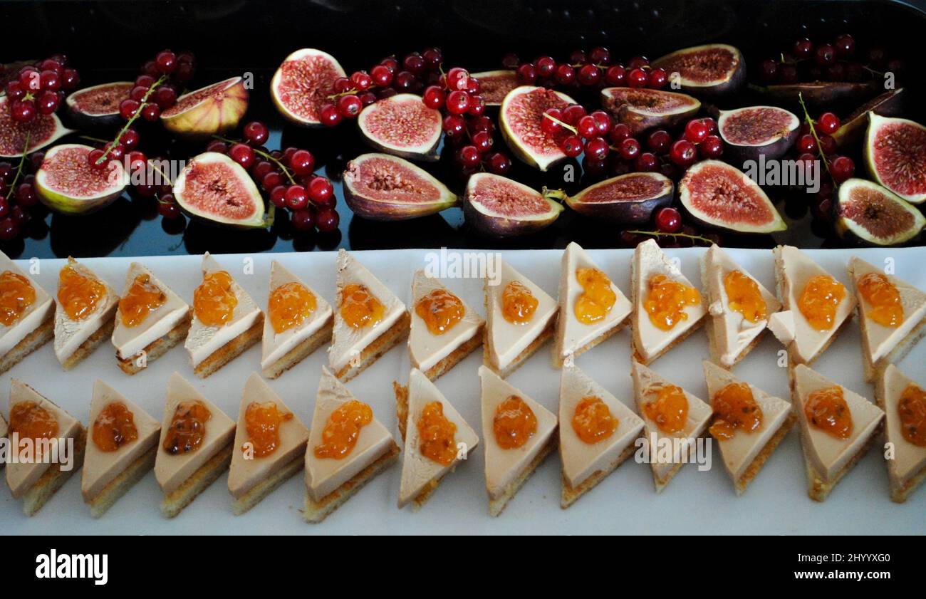 Canapés de foie gras recouverts de confiture de myrtilles et hors d'œuvre sur un plateau décoré de figues et de raisins de Corinthe rouges. Banque D'Images