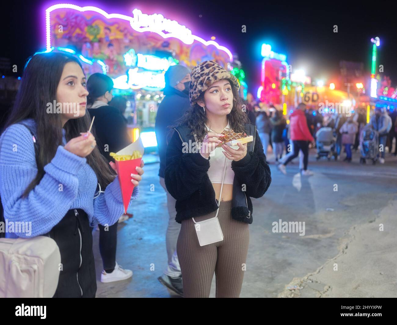 Distrait les femmes mangeant des frites et des gaufres debout lors d'une foire nocturne Banque D'Images