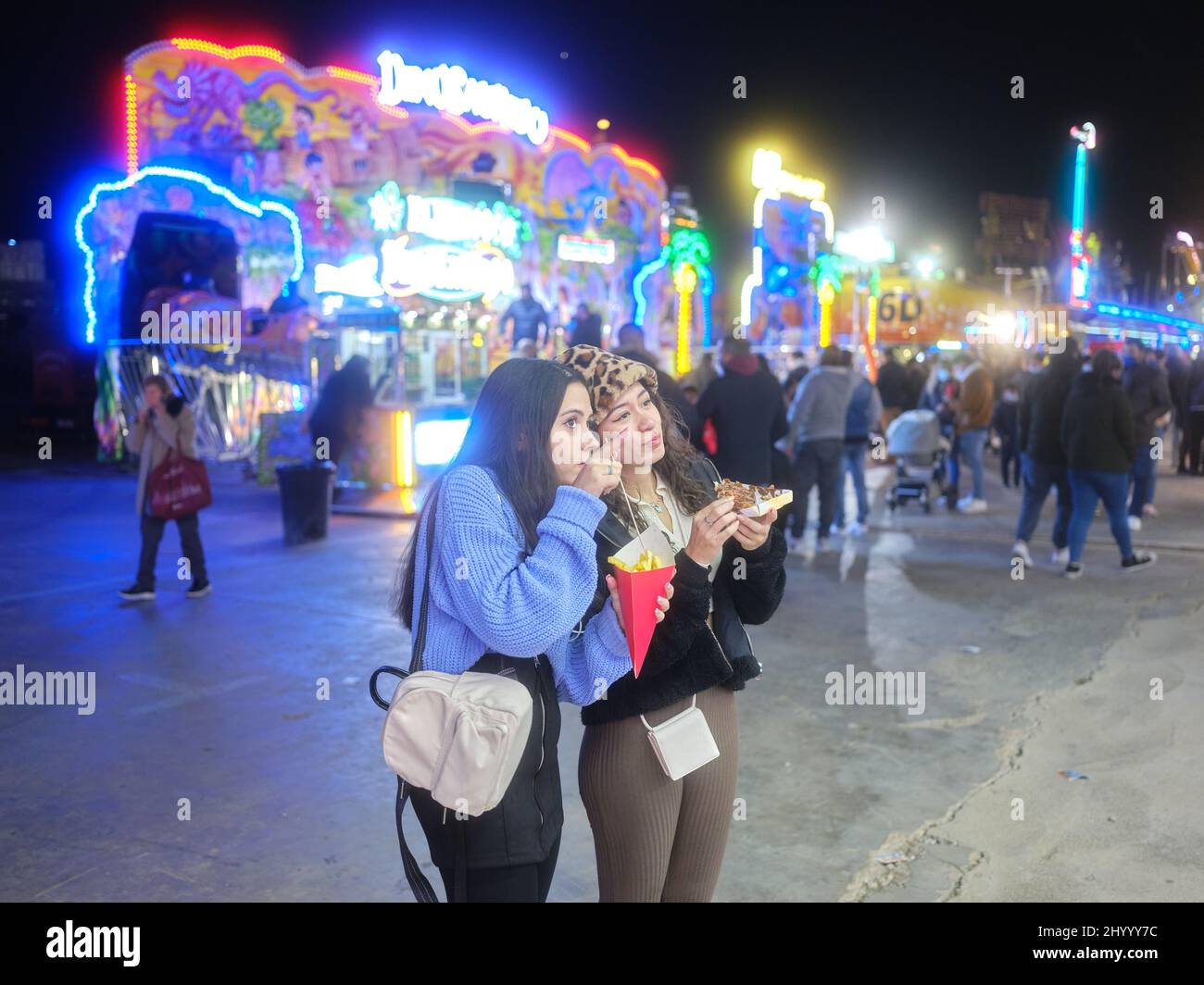 Fille pointant vers l'avant et parlant à un ami et manger à une foire la nuit Banque D'Images