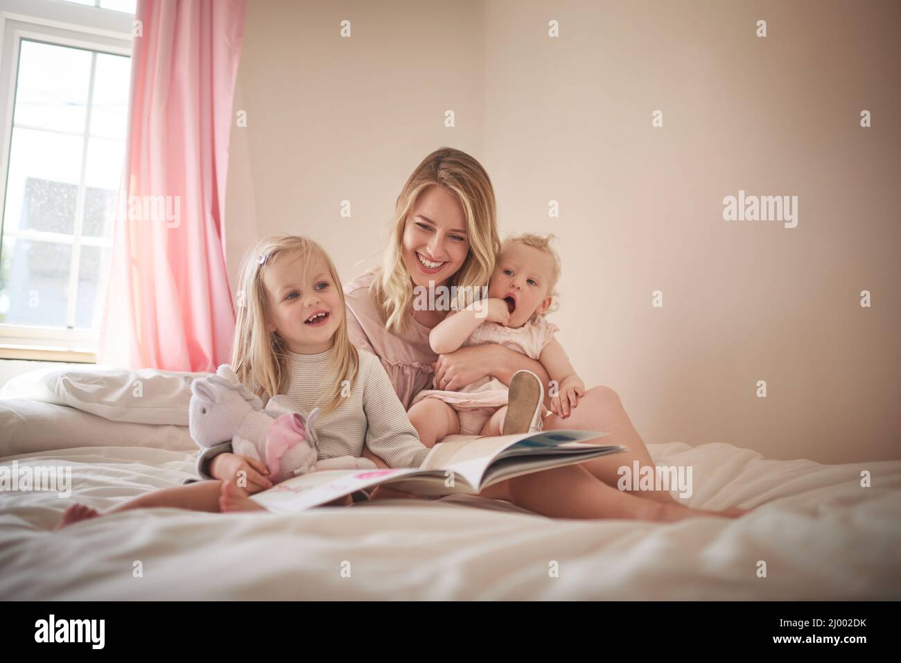 Les histoires sont amusantes pour toute la famille. Photo d'une adorable famille de trois personnes lisant un livre ensemble sur le lit à la maison. Banque D'Images