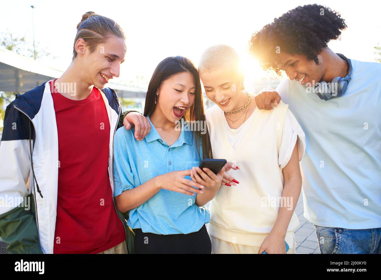 Regrouper des jeunes multiraciaux à l'aide d'un smartphone mobile en extérieur, ils regardent quelque chose avec un visage surpris. Millénaire multiethnique Banque D'Images