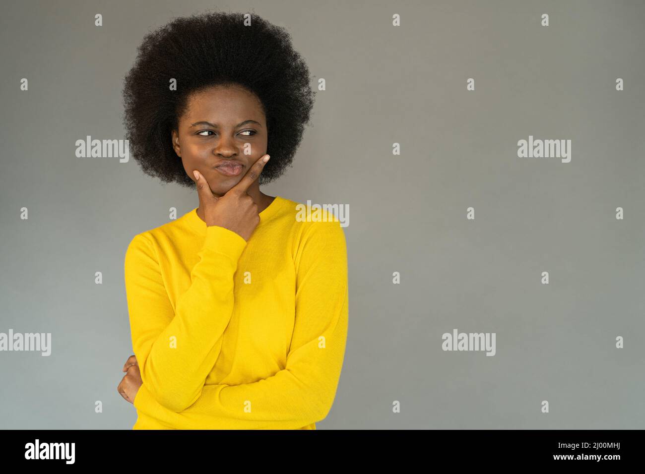 Une jeune femme africaine douée touche son menton, sceptique et pensive pense à l'espace de copie Banque D'Images