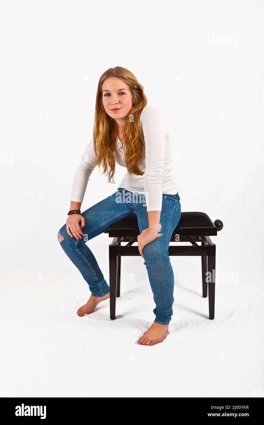 Portrait en longueur de la belle fille heureuse assise sur un fauteuil de piano, isolée sur fond blanc Banque D'Images