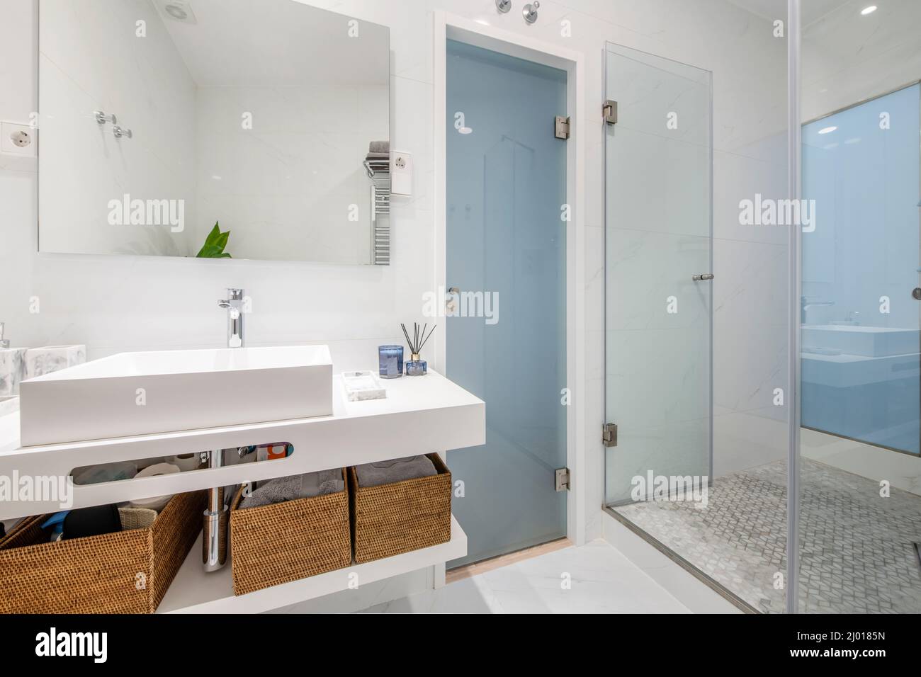 salle de bains avec éléments en porcelaine blanche murs carrelés de blanc et sols en marbre, porte-serviettes chauffant en acier inoxydable et cabine de douche avec cloison en verre Banque D'Images
