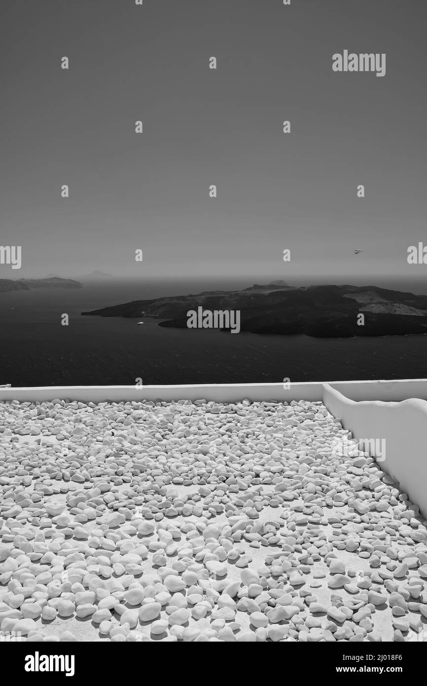 Vue sur le volcan de Santorin depuis un toit rempli de pierres en noir et blanc Banque D'Images