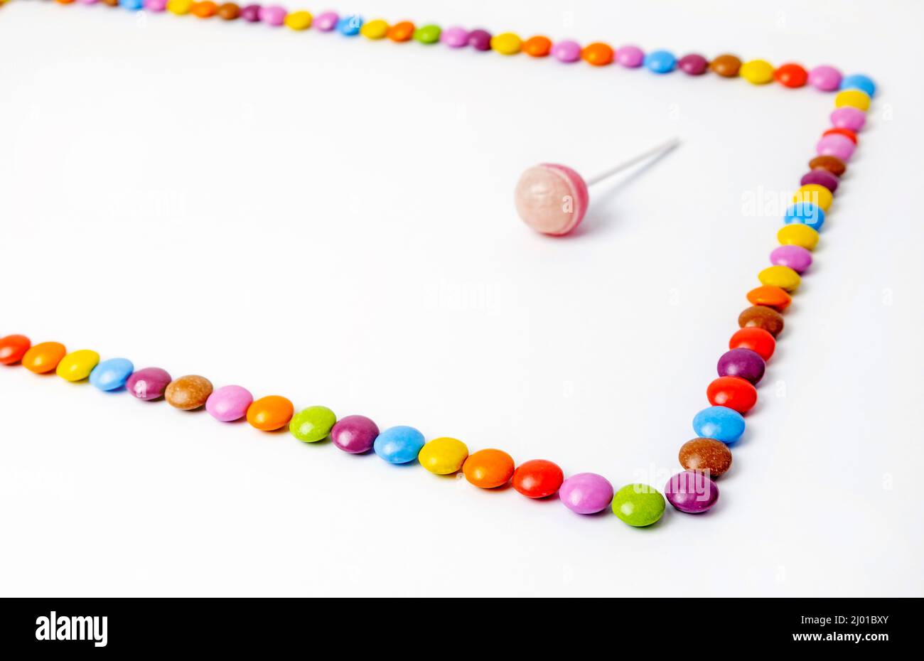 Dragées de chocolat bordées de rectangle sur fond blanc. Cadre de bonbons colorés avec sucettes. Banque D'Images