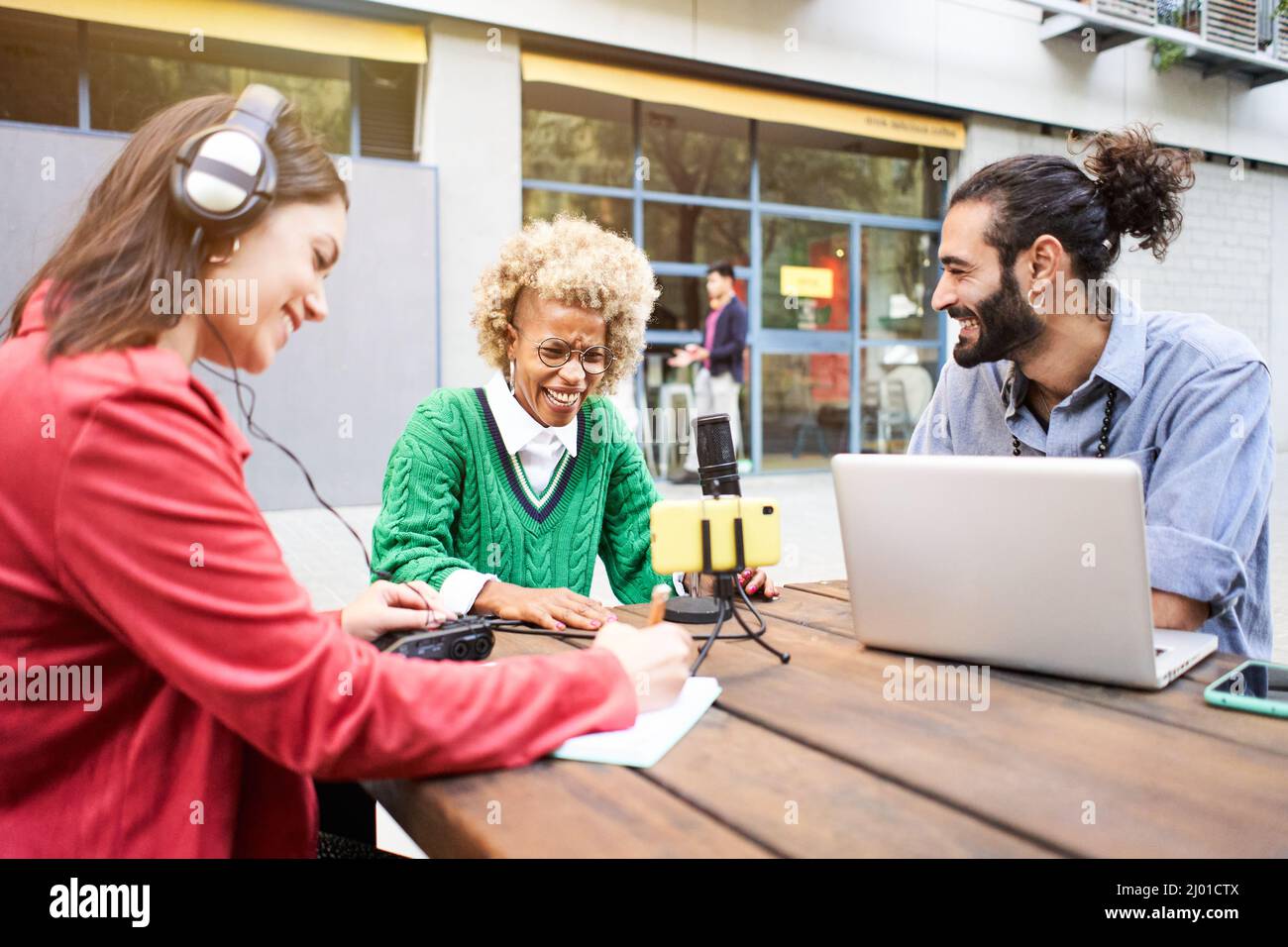 Jeune femme interviewant un homme dans un studio de radio décontracté à l'extérieur. Les gens du millénaire qui utilisent la technologie, les ordinateurs, les casques, le micro... Banque D'Images