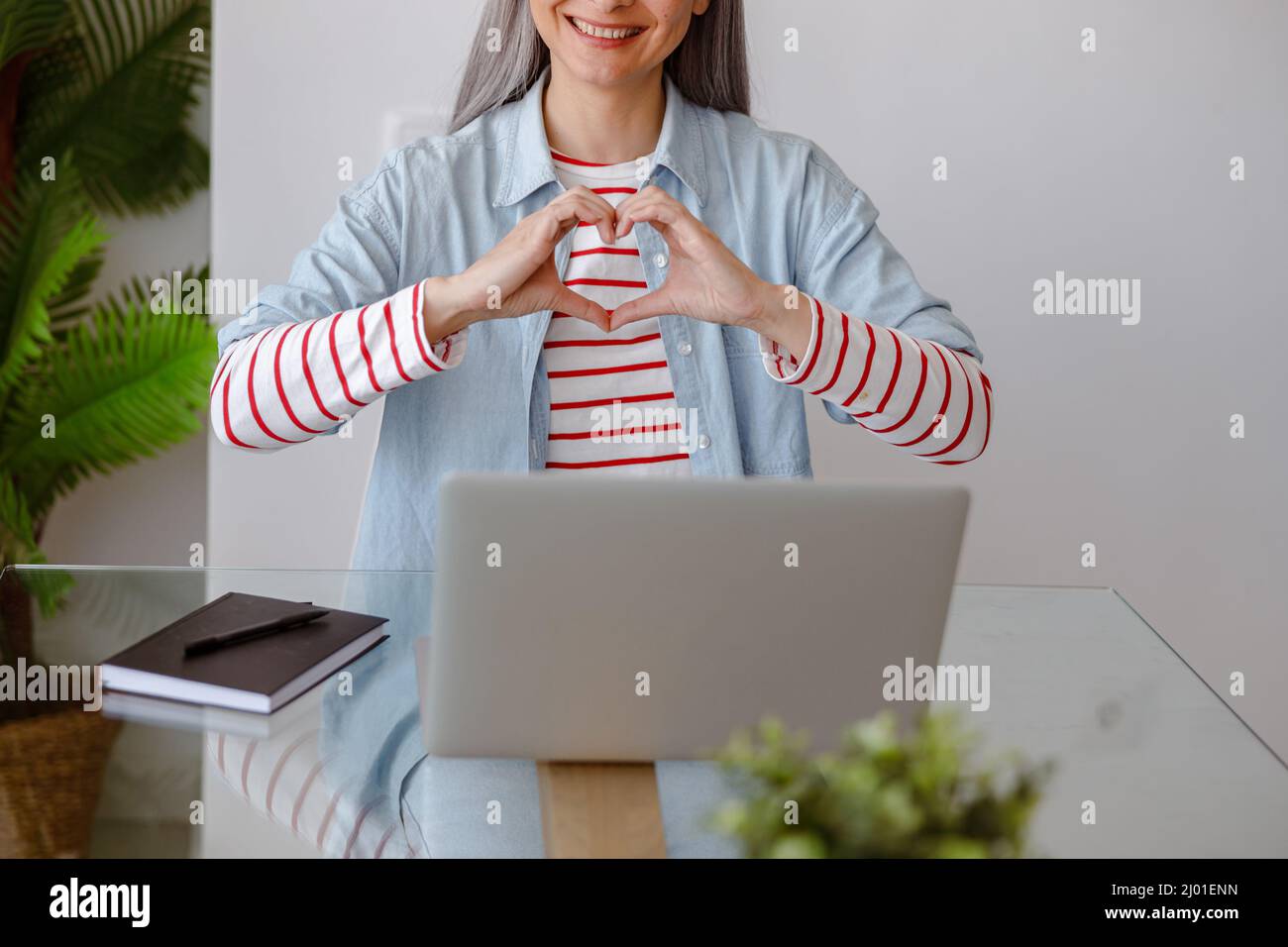 Femme assise à la table avec un carnet et faisant un geste de coeur Banque D'Images